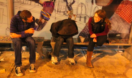 three people sitting on a bus stop bench