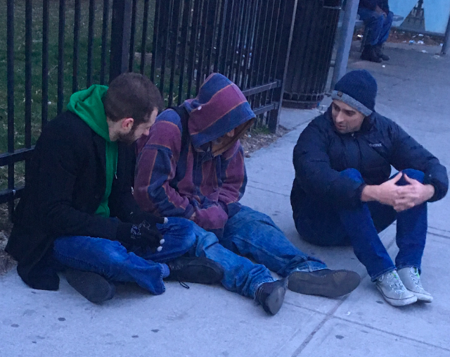 three people sitting on the sidewalk