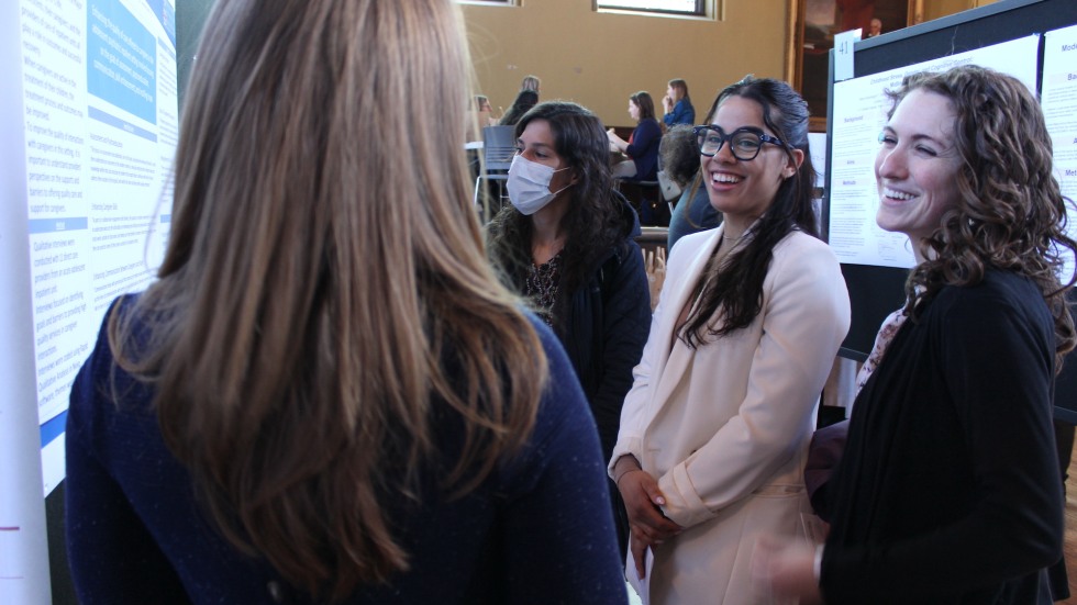 person stands beside a poster with three people looking on